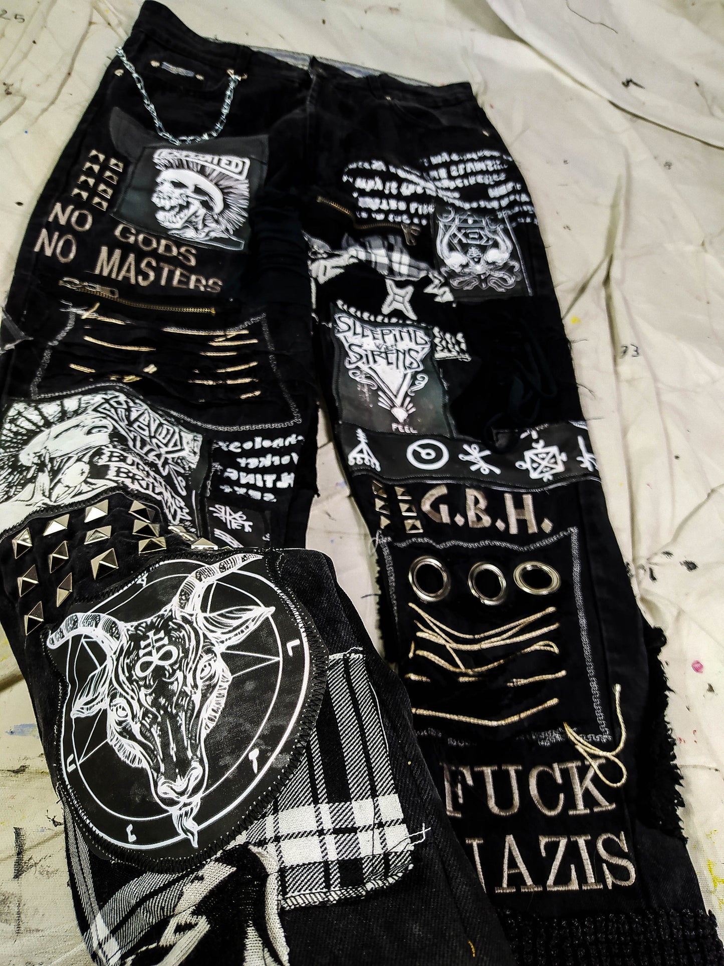Flat laid black pair with embroideries such as no gods, no masters, prints with punk bands such as exploited, burning britain, sleeping with sirens along with studs, goat with horns, eyelets, laces, zippers, chain, abstract paint and patchwork.