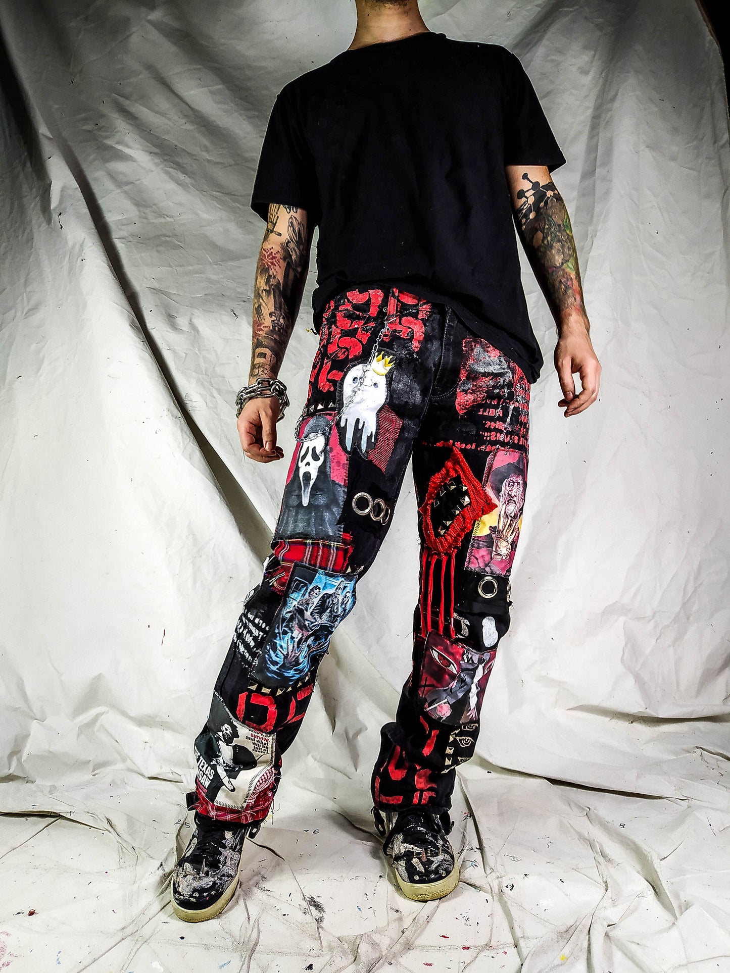 Model showing a custom made black pair with prints containing various horror movies, red and black patchwork, abstract painting, studs, red laces hanging down, chain and eyelets.