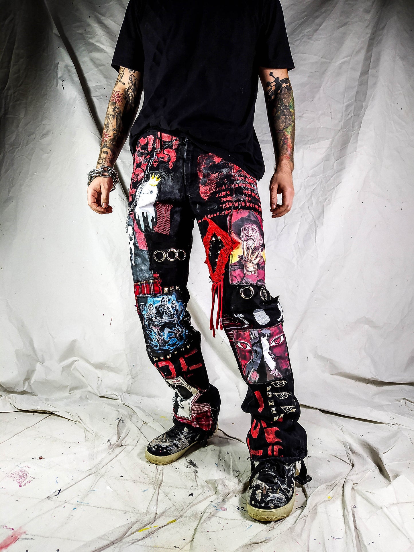 Model showing a custom made black pair with prints containing various horror movies, red and black patchwork, abstract painting, studs, red laces hanging down, chain and eyelets.