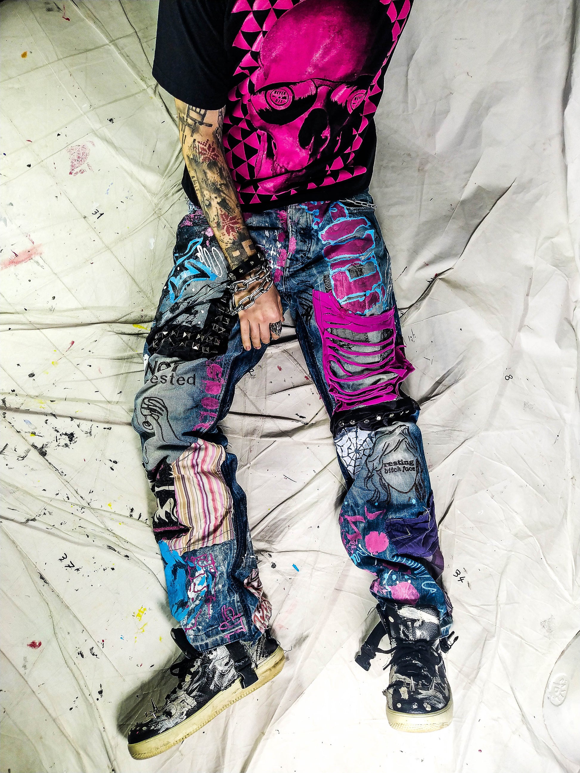 Model wearing the blue pants with abstract one line embroideries representing women saying I&#39;m not interested on one leg and Resting bitch face on the other. Colorful patchwork with add ons such as studs, zippers and elastic laces hanging down.