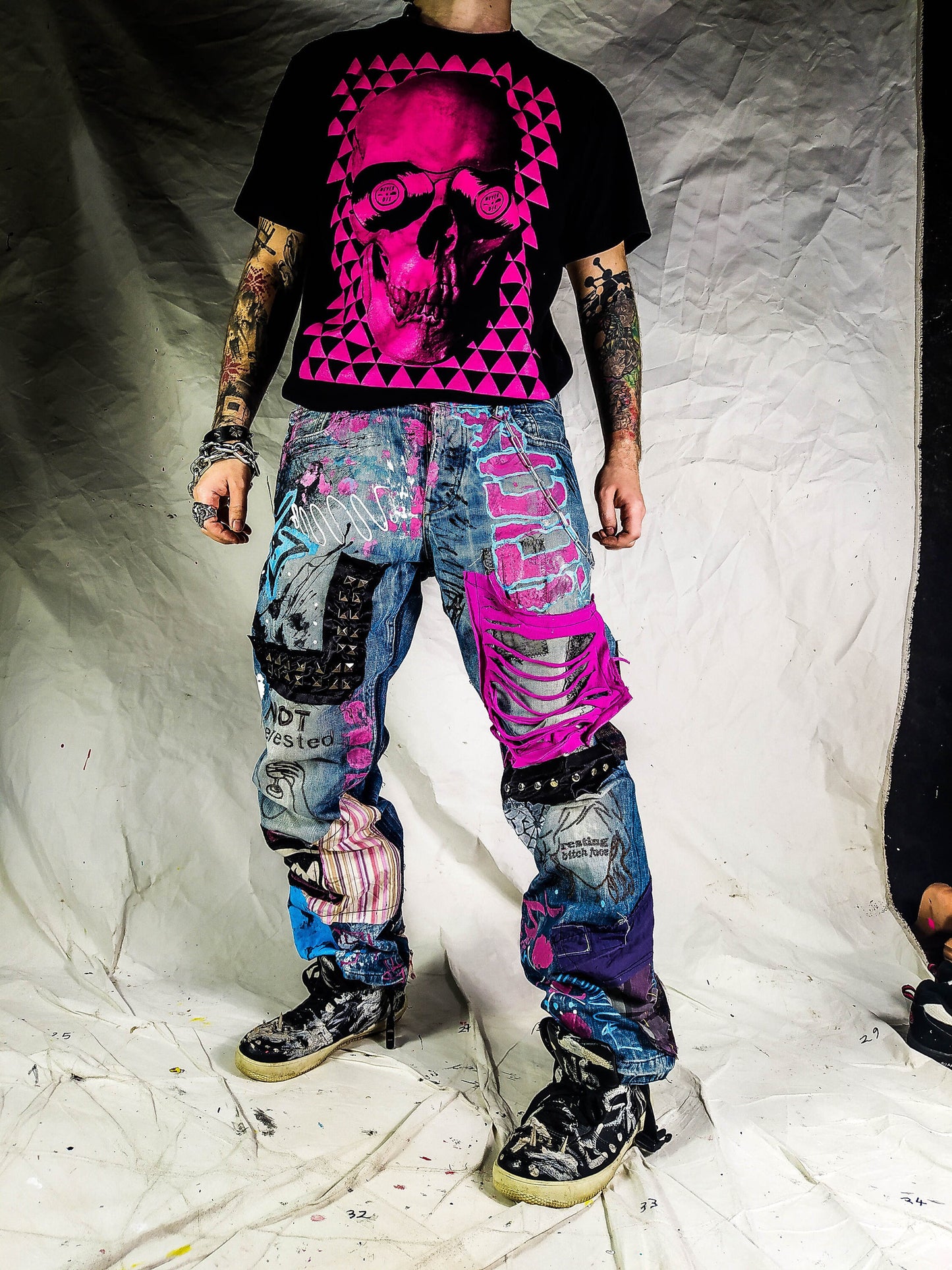 Model wearing the blue pants with abstract one line embroideries representing women saying I&#39;m not interested on one leg and Resting bitch face on the other. Colorful patchwork with add ons such as studs, zippers and elastic laces hanging down.