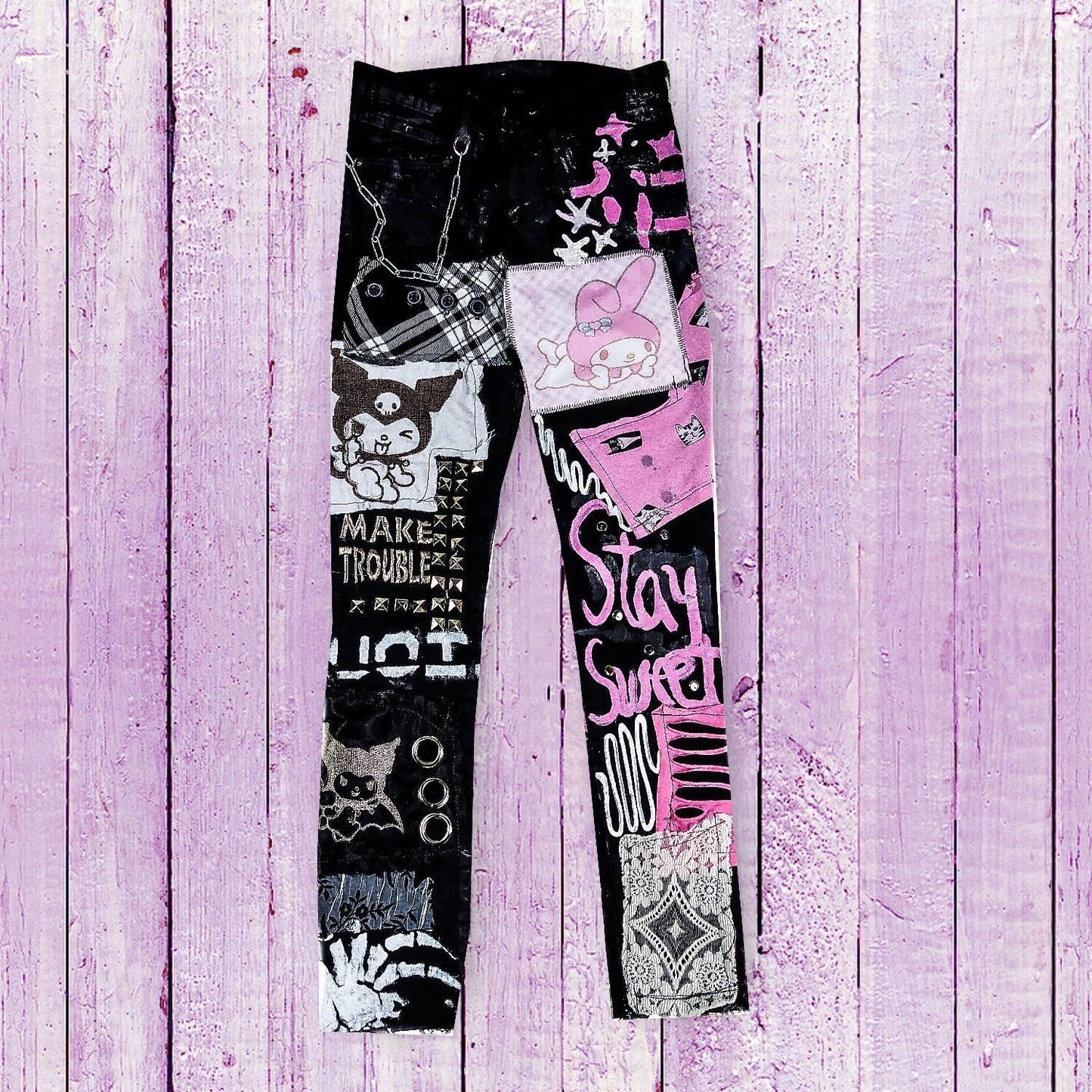 Flat laid black skinny pair with kuromy and my melody as embroidered and printed, with embroidered and painted writings such as stay sweet and make trouble, abstract pink and white patchwork, studs, rivets, painted stars and hearts, chain.