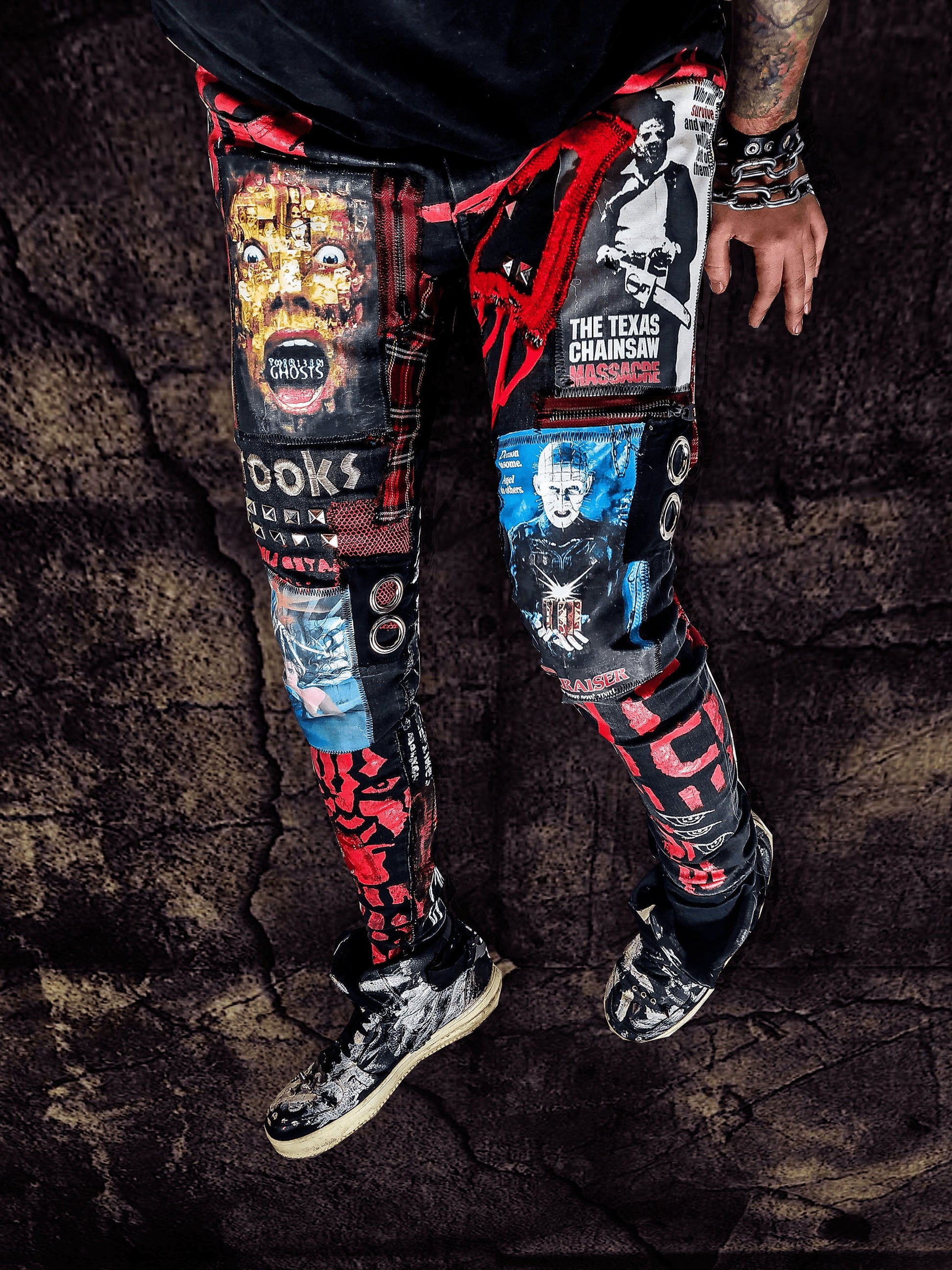 Model showing a skinny custom made black pair with prints containing various horror movies, red and black patchwork, abstract painting, studs, red laces hanging down, chain and eyelets.