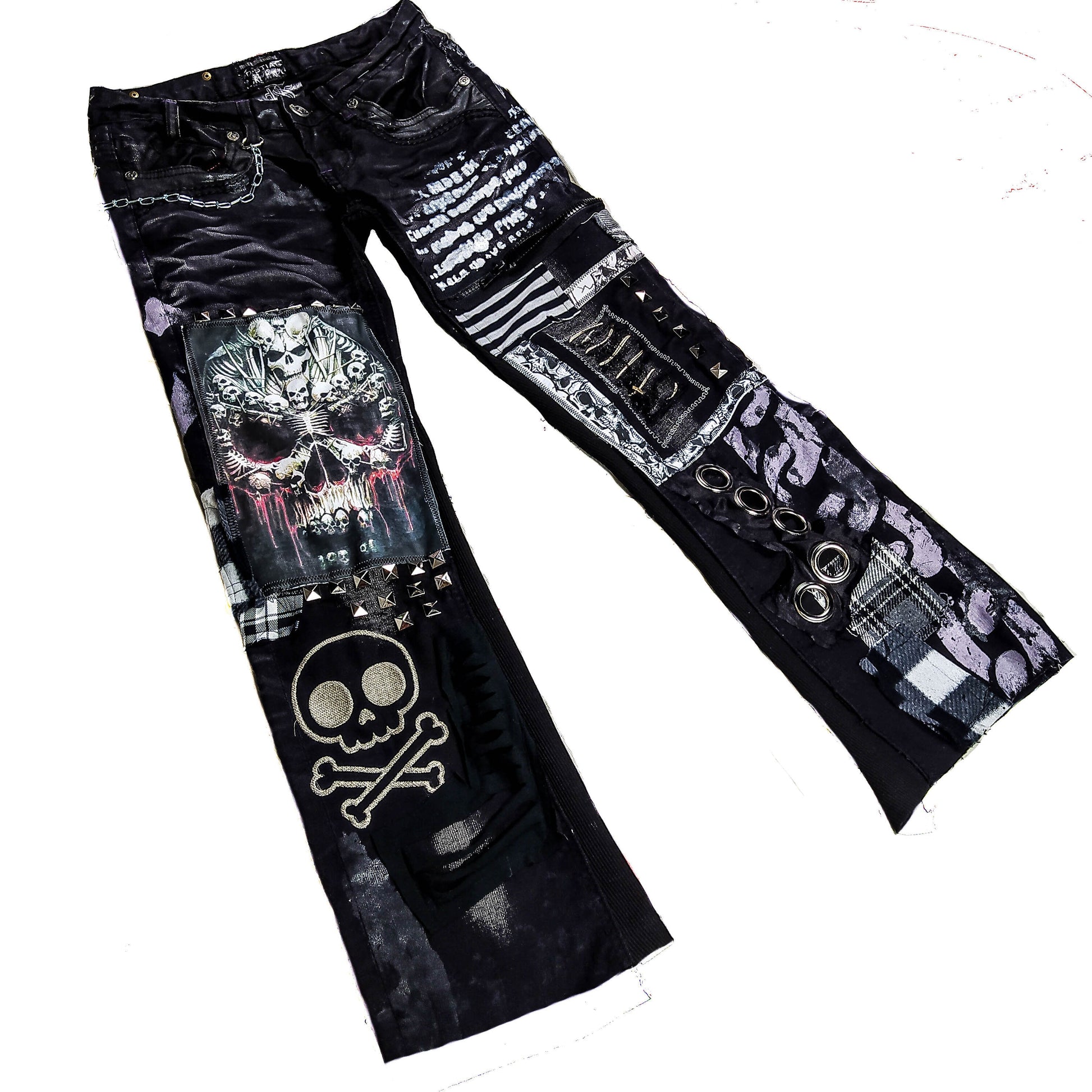 Flad laid black pair of pants with printed and embroidered skulls, eyelets, studs, chain and abstract patchwork and painting in gray, black and white.