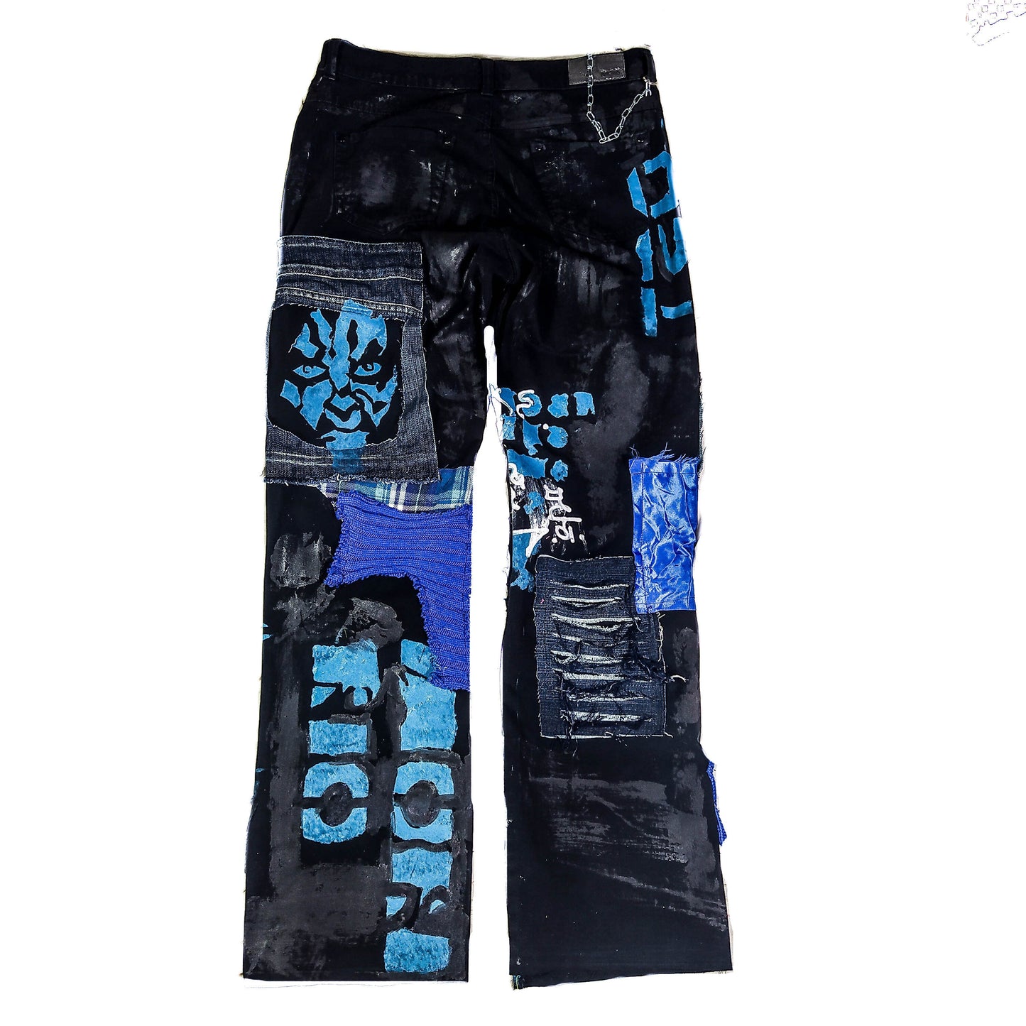 Flat laid black pants with anime prints, colorful patchwork in multiple blue shades, ripped patches, zipper, eyelets, studs and abstract painting with a blue snake on the front.