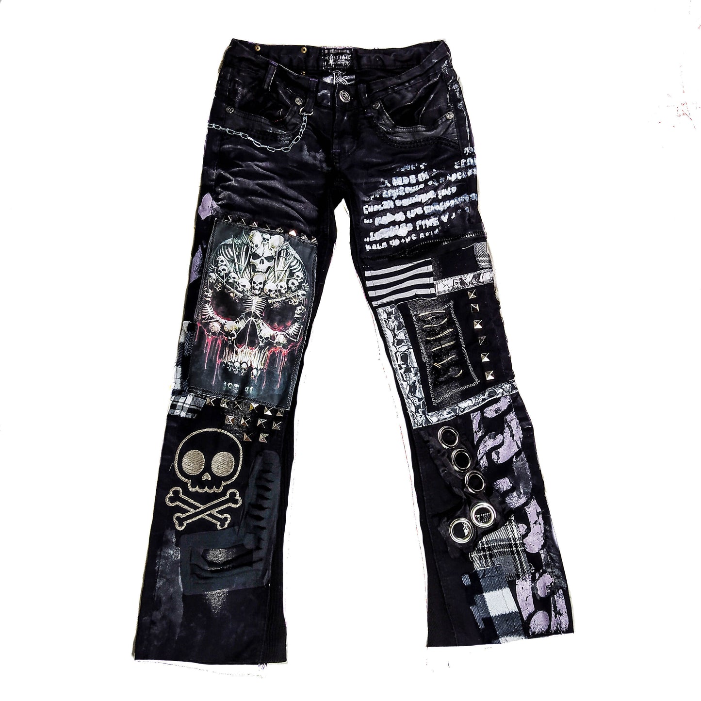 Flad laid black pair of pants with printed and embroidered skulls, eyelets, studs, chain and abstract patchwork and painting in gray, black and white.